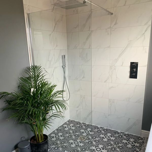 Modern bathroom shower with glass partition and patterned floor tiles.