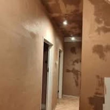 A hallway with unfinished plaster walls and ceiling under construction.