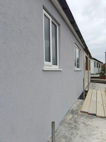 A gray building wall with white windows under a cloudy sky.