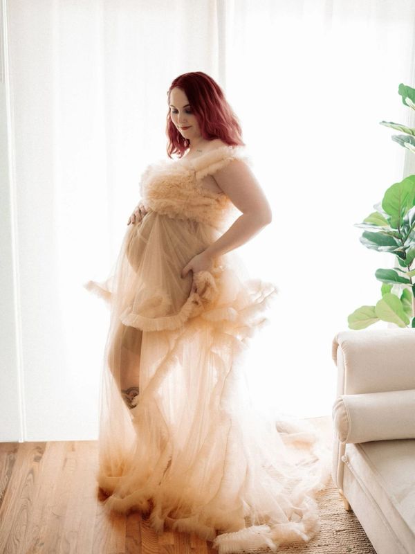 Pregnant woman in a flowing beige dress gently holding her belly.
