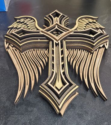 Intricately layered wooden cross with wing designs on a black surface.