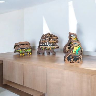 Wooden bear-shaped layered art pieces with nature scenes inside, displayed on a wooden cabinet.