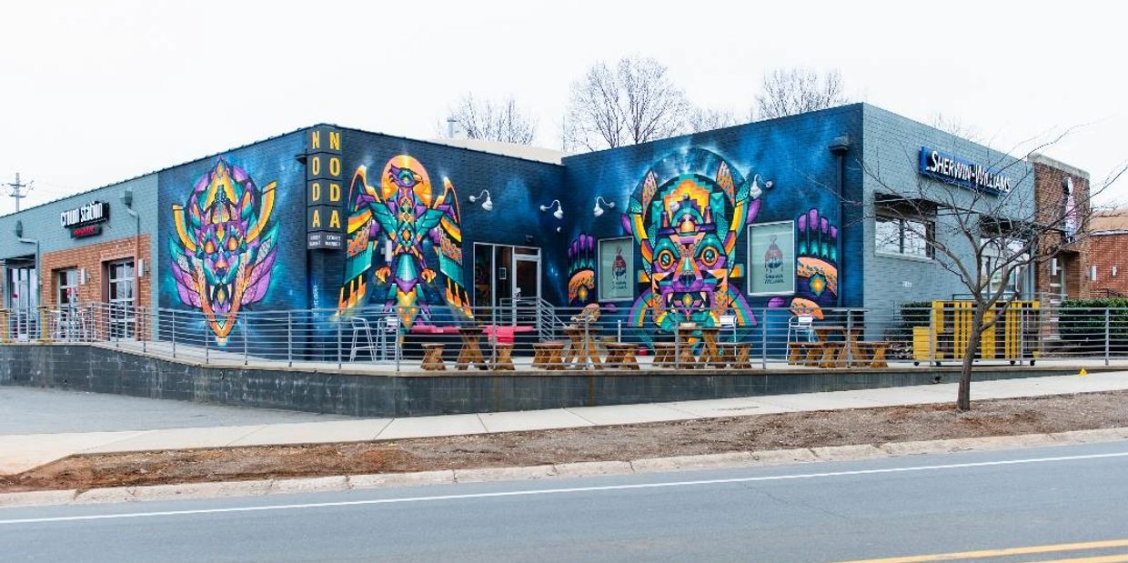 A warrior, a phoenix, and a jaguar painted on a blue background on three wall sof a building.
