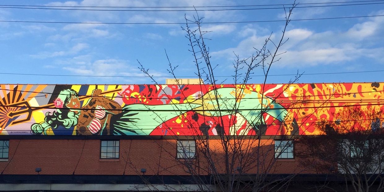 Mural with a mermaid in an horizontal position and tattoos on her upper body holding a trident.