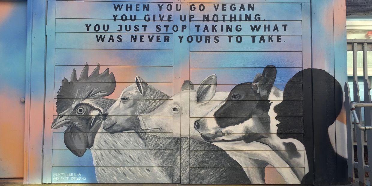 Mural with rooster, sheep, pig, and cow in grays and a human profile on a blue and pink background.