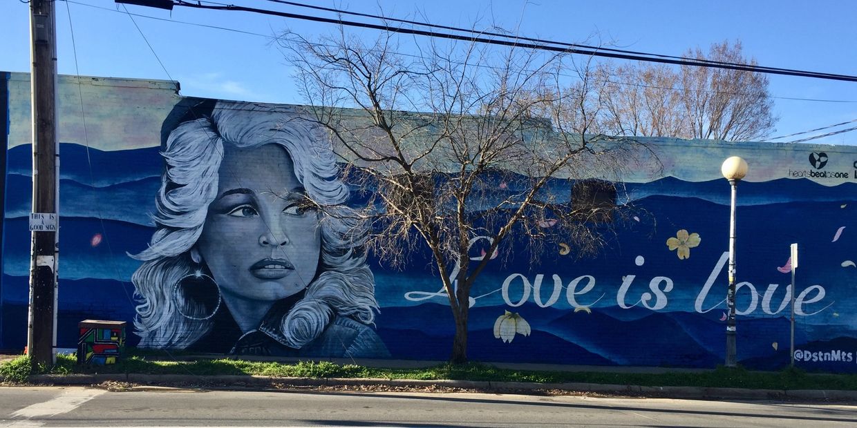 Mural with Dolly Parton portrait, blue mountain ranges in background and Love is Love in text
