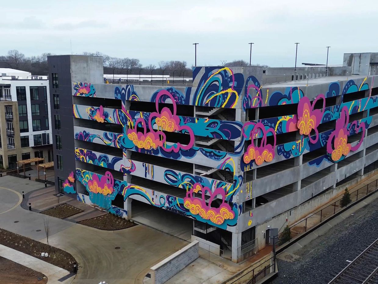 A six story parking deck mural with blue, pink, and yellow large, cloud shapes along two sides.