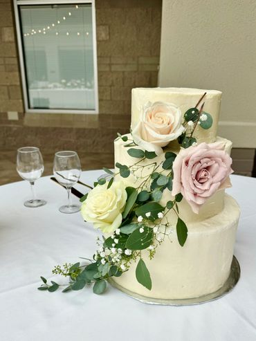 White 3 tiered wedding cake with roses and greenery trailing down the cake
