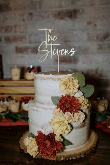 White naked wedding cake with orange and white flowers and a cake topper