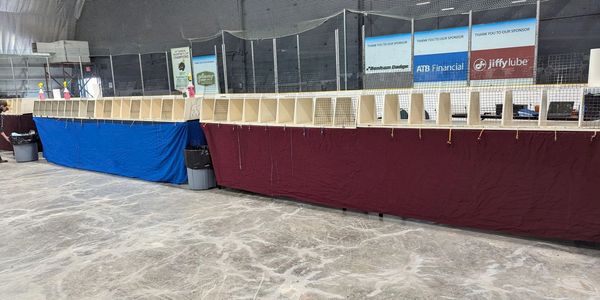A long, empty wooden stall stands inside an ice rink, covered with blue and maroon cloths.