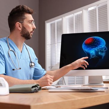 Male doctor pointing to an image of a brain scan on a computer.