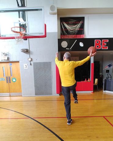 Man in yellow shirt practicing basketball shot in gym.
