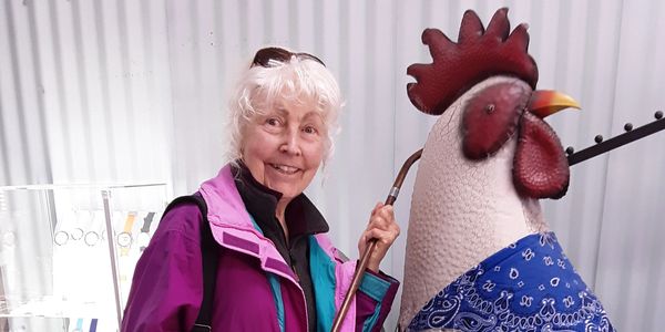 Dianne Erickson standing next to a large metal Rooster. 