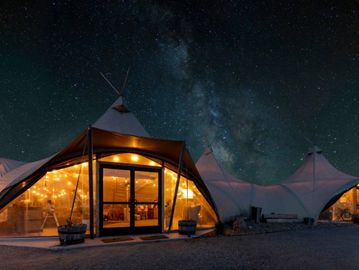 Glowing tents under a starry night sky with the Milky Way visible.