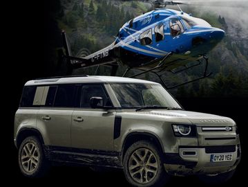Land Rover Defender SUV with a blue helicopter in a mountainous background.