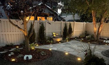 Cozy backyard garden with illuminated pathway and trees at dusk.