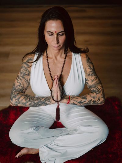 Tattooed woman in white meditating with hands in prayer pose.