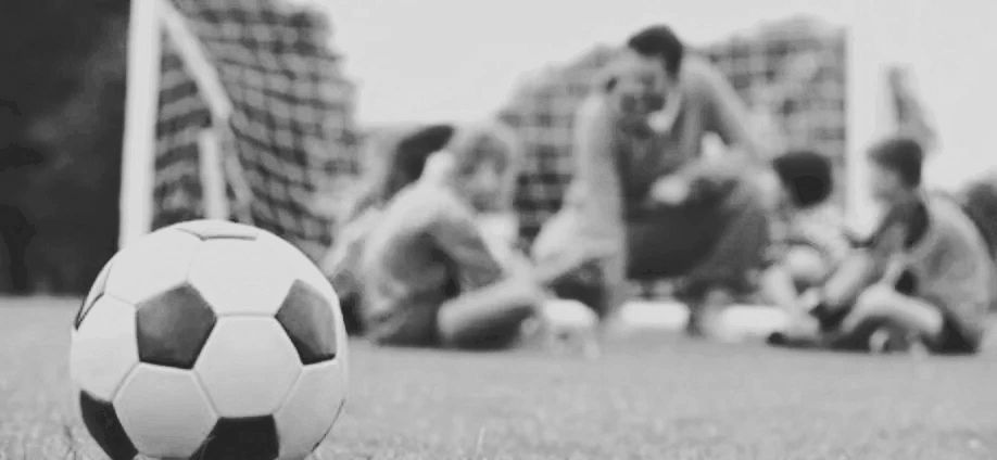 Soccer ball with kids and coach in background.