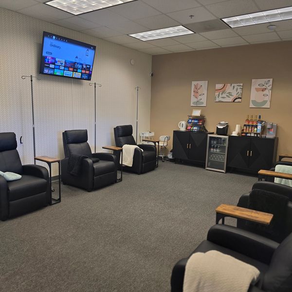 Cozy waiting room with black leather chairs, TV, and refreshment station.