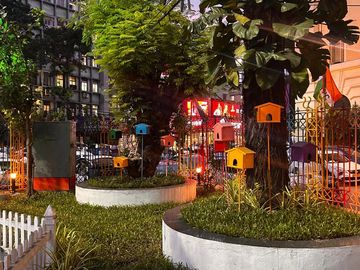 Colorful birdhouses decorate a small urban garden at dusk.