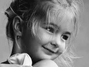 A young ballet dancer hugging her shoes with a smile.
