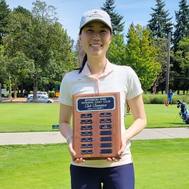 A young woman holding a golf club champion plaque outdoors.