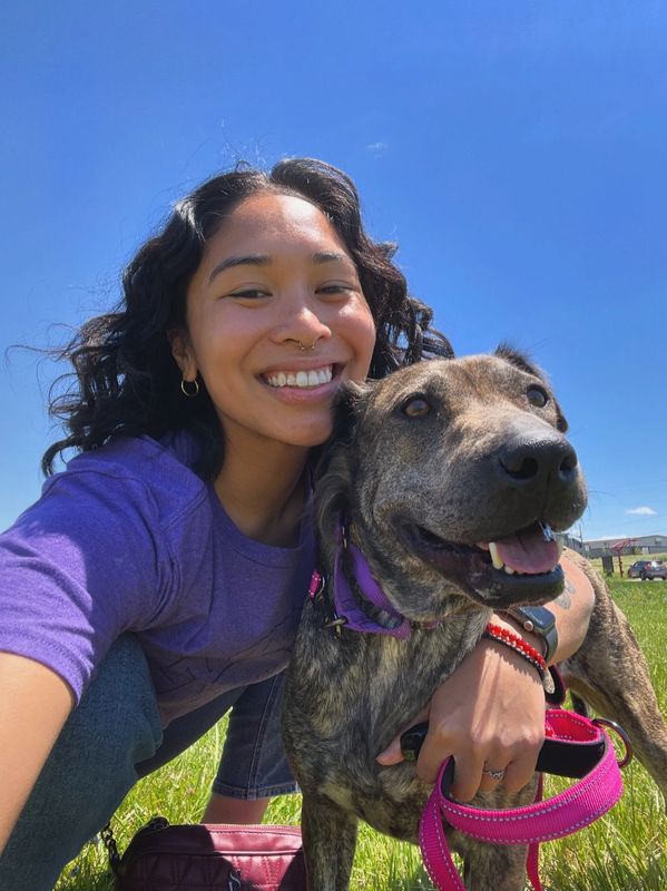 Smiling woman with a dog outdoors on a sunny day.