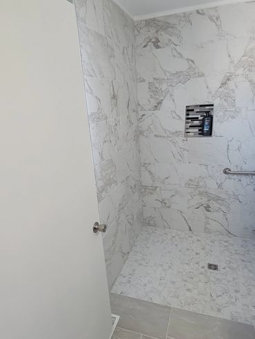 Modern bathroom shower with marble tiles and built-in shelf.