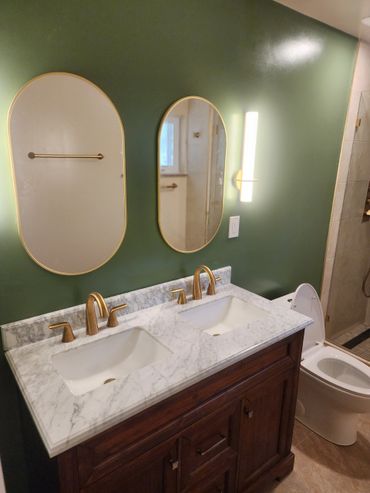 Modern bathroom with double sinks, gold fixtures, and green wall.