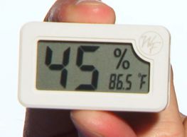 A humidity gauge being held between an index finger and a thumb
