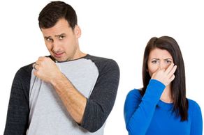 Male holding the collar corner of his T-shirt to his nose with a disgusted expression, and a female