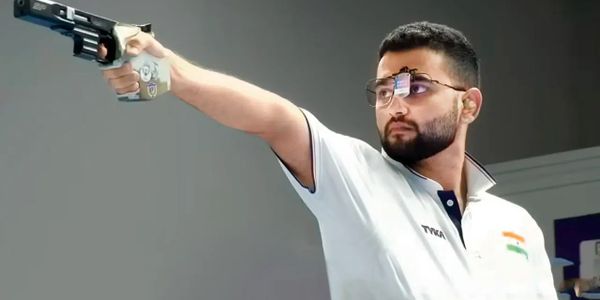Man aiming a pistol in a shooting competition, wearing protective eyewear.