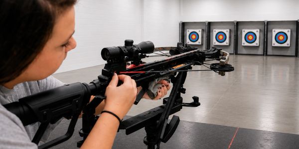 Person aiming a crossbow at targets in an indoor shooting range.