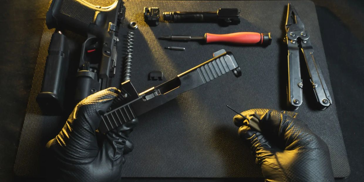 Person assembling a handgun with tools on a black mat.