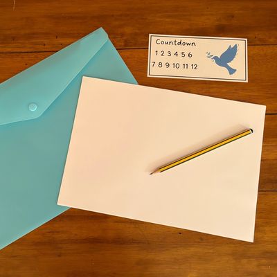 Blank paper, yellow pencil, blue envelope, and a countdown card on wooden surface.