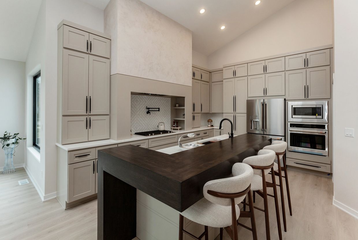 Modern kitchen with beige cabinets, dark wood island, and bar stools.