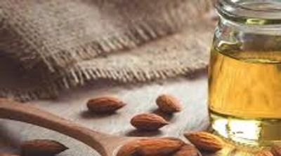 Glass of Organic Sweet Almond Oil and almonds on table and in wooden spoon