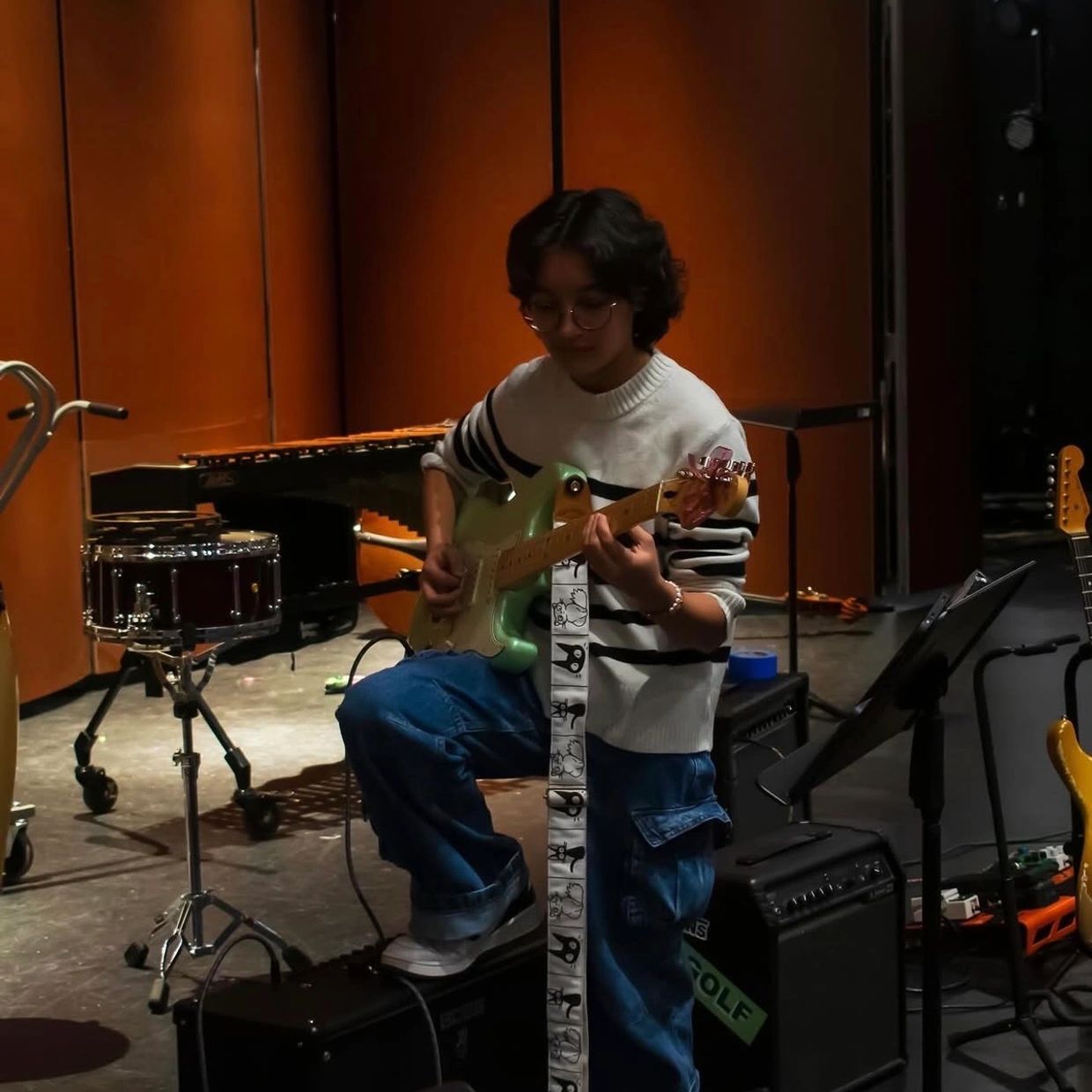 Person playing electric guitar in a music room with various instruments.