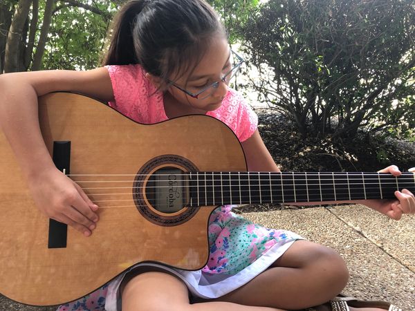 Young girl focused on playing an acoustic guitar outdoors.