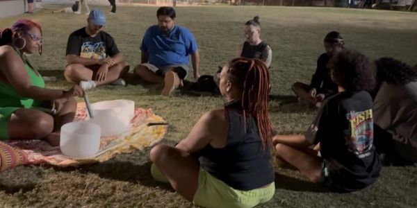 Group sits on grass in a circle outdoors at night.