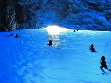 People swimming in a glowing blue cave pool.