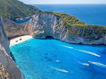 Bright blue bay surrounded by cliffs with boats near a sandy beach.
