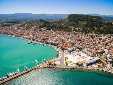 A coastal town with turquoise waters, boats, and a mountainous backdrop under clear blue skies.