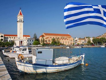 Fishing boats docked in a Greek harbor with a waving Greek flag.