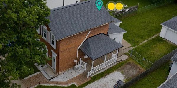 A brick house with a gray roof and white porch in a green yard.