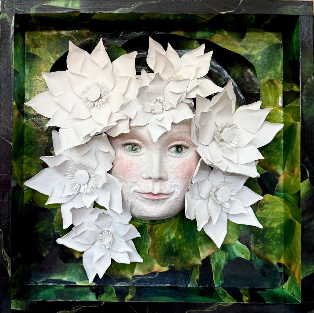 Sculpted face surrounded by large white flowers in a green leafy frame.