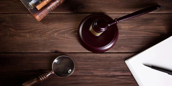 Judge's gavel, magnifying glass, and notebook on wooden table.