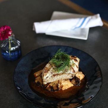 Grilled fish fillet garnished with fresh herbs on a dark plate.