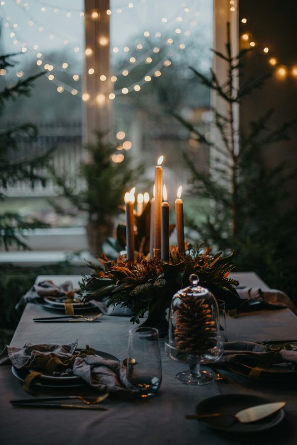 Cozy indoor holiday table setting with lit candles and festive decorations. Christmas Decor