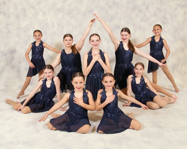 Young girls in navy blue dance costumes posing for a group photo.